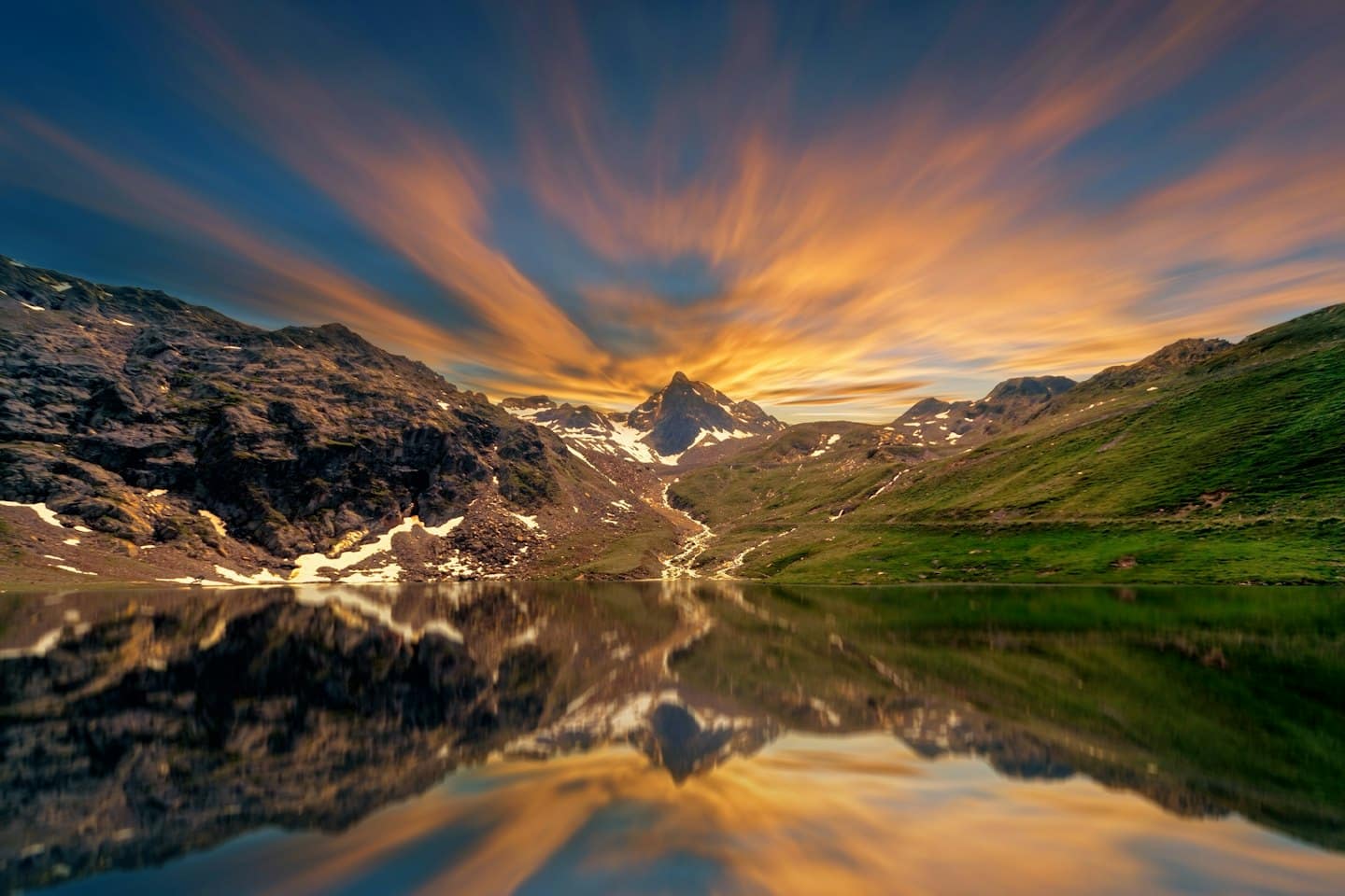 Montagne frastagliate e neve si riflettono in un lago alpino.