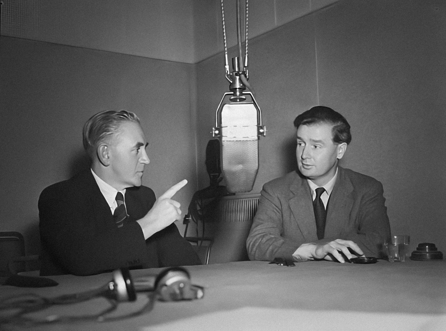Due uomini parlano in un microfono durante una trasmissione radiofonica.
